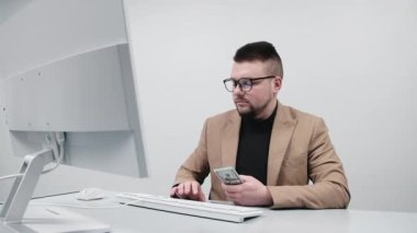 Gözlüklü genç bir girişimci modern bir ofiste nakit sayar. Konsept bir anlık finansal başarı, kazanç ve iş amaçlarına ulaşmak..