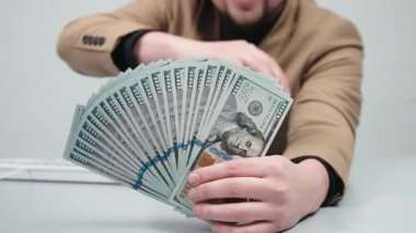 Gözlüklü genç bir işadamı modern bir ofiste elinde büyük miktarda nakit para tutuyor. Konsept, finansal bağımsızlığı ve iş hayatında başarıyı elde etmenin hissini aktarmak..