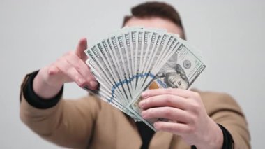 Gözlüklü genç bir işadamı modern bir ofiste elinde büyük miktarda nakit para tutuyor. Konsept, finansal bağımsızlığı ve iş hayatında başarıyı elde etmenin hissini aktarmak..