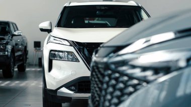 Modern araba galerisi ön planda, modern otomotiv estetiği ve stilini ön plana çıkaran, bulanık araçlı, parlak beyaz bir SUV sergiliyor.