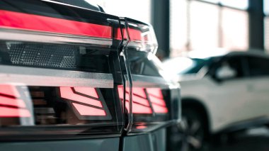 Çağdaş bir arabanın arka lambasına yakın çekim, parlak tasarımını ve parlak kırmızı ışığını vurguluyor, sofistike bir sergi salonu atmosferinde ayarlanıyor.