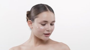 Genç bir kadın yüzüne nemlendirici krem sürüyor.