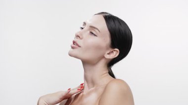 Beyaz arka planda poz verirken kadın boynuna dokunuyor