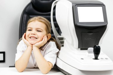 Gülümseyen kız göz muayene makinesinin yanında oturuyor.