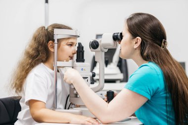 Pediatrik bir göz doktoru küçük bir kızın gözlerini inceliyor. Oftalmik enstrüman. Dikkatli tanı ve çocukların göz sağlığı için bakım.