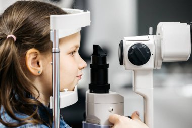 Genç bir kız ileri düzey göz teçhizatıyla göz muayenesine katılıyor, pediatrik göz bakımının önemini vurguluyor ve klinik bir ortamda görme sağlığı bilincini destekliyor.