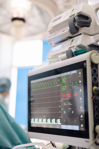 Хирургическое оборудование мониторинга показывает жизненно важные показатели в операционной, с медицинскими работниками на заднем плане, подчеркивая уход за пациентами и безопасность во время хирургических процедур