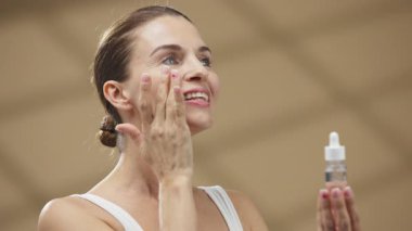 Gülümseyen kadın yüzüne krem sürüyor.