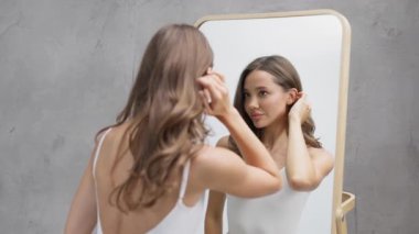 Genç bir kadın aynaya bakarken saçlarını düzeltiyor.