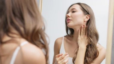 Ayna yansımasında pürüzsüz cildi inceleyen genç bir kadın.