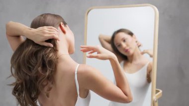 Aynadaki yansımaya bakarken saçları düzelten kadın.