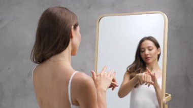 Aynanın yanında duran bir kadın losyon sürüyor.