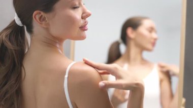 Çıplak omzuna hafifçe losyon süren kadın.