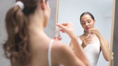 Aynanın yanında elinde parfüm şişesi tutan bir kadın.