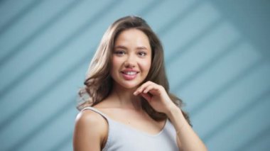 Gülümseyen genç kadın mavi arka planda poz veriyor.