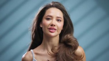 Gülümseyen genç kadın mavi arka planda poz veriyor.