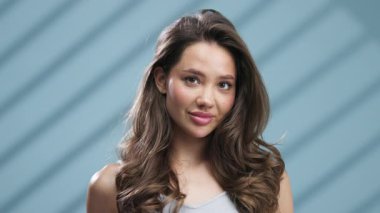 Gülümseyen genç kadın mavi arka planda poz veriyor.