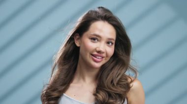 Gülümseyen genç kadın mavi arka planda poz veriyor.