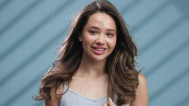 Gülümseyen genç kadın uzun kahverengi saçlara dokunuyor.