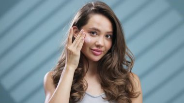 Yanağına krem süren genç bir kadın gülümsüyor.