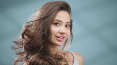 Gülümseyen genç kadın mavi arka planda poz veriyor.