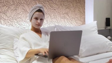 Yüz maskesi takan kadın dizüstü bilgisayar yatağı kullanıyor.