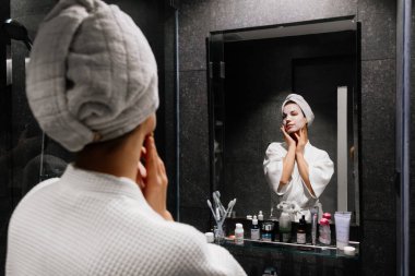 Aynaya krem süren havlu giymiş bir kadın.