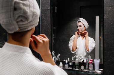 Aynaya bakarken yüz maskesi takan kadın.