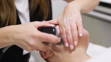 Estetisyen modern cihaz kullanarak yüz bakımı yapıyor.