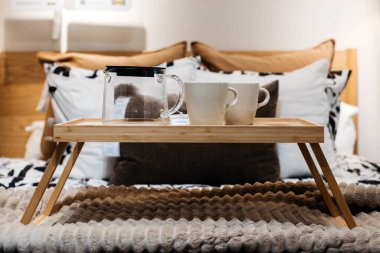 Tahta kahvaltı tepsisinde fincanlar ve çaydanlık var.