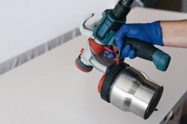 Eldivenli, elinde elektrikli boya spreyi aleti var.