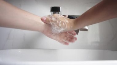 Lavaboda akan suyun altında ellerini yıkamak.