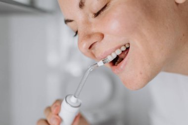 Gülümseyen kadın, diş ipi kullanarak dişlerini temizliyor.