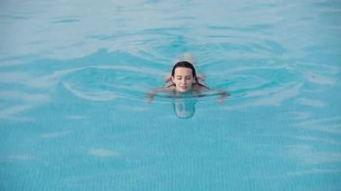Açık mavi yüzme havuzunda yüzen kadın