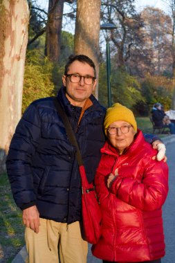 Man with his elderly mum walking along the park