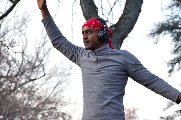 Focused Black man training at the park walking the rope with red bandana and earphones.