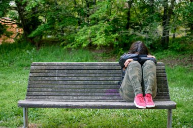 Genç bir kadın ve depresyonda. Parktaki bankta tek başına oturuyor. Kolları ve başı dizlerinde. Üzüntü, yalnızlık ve kişisel sorunlar kavramı