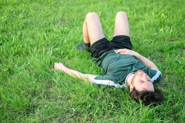 stock image Image of young man with green t-shirt lying on grass in park after exercising exhausted