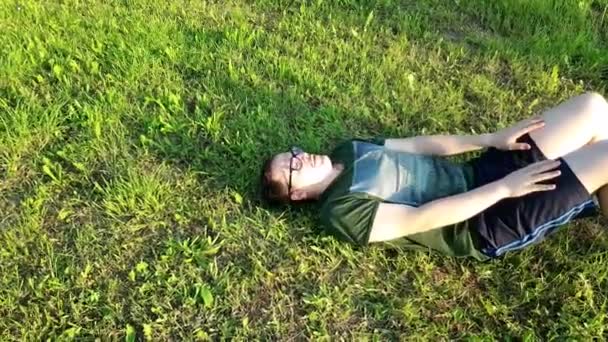 Молодий Чоловік Окулярах Зеленій Футболці Сидить Парку Травою Сонячним Днем — стокове відео