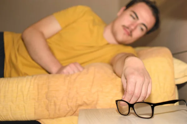 Νεαρός Άντρας Κρατάει Γυαλιά Του Καθώς Σηκώνεται Από Κρεβάτι Αμυδρό — Φωτογραφία Αρχείου