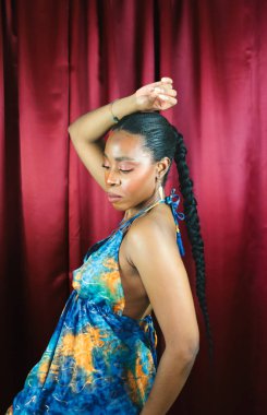 Mavi elbiseli, kırmızı arka planda dans eden ve gülümseyen Afrikalı kadın etnik kökenli.