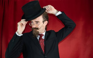 Silindir şapkalı, gözlüklü ve kırmızı arkaplanlı bıyıklı klasik Kafkas Sihirbazı.