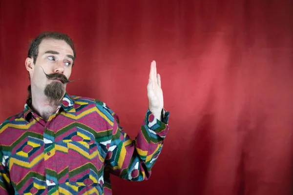 Hipster man moving head and saying No or Stop to his left side with open hand with red background