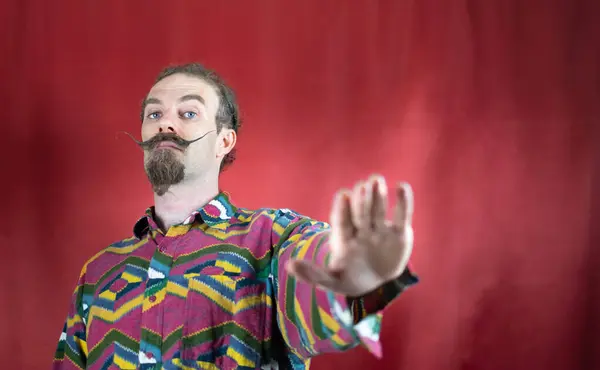 Hipster man with mustache saying No or Stop and looking at camera with open hand and red background