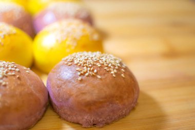 Ahşap zemin üzerinde susam tohumları olan eğlenceli renkli hamburger çörekleri.