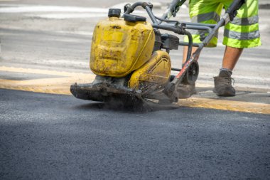 Operatörün sokakta asfaltı sarı otomatik silindirle yıkarken görüntüsü