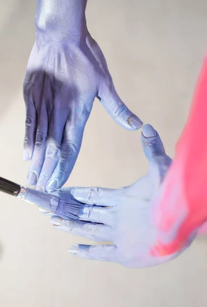 Close up image of female model hands being painted for body painting show in blue and pink color