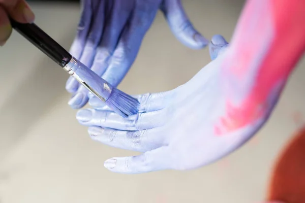 Close up image of female model hands being painted for body painting show in blue and pink color