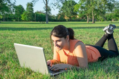 Kafkasyalı genç bir kadının laptopuyla parkta yatması çok mutlu bir görüntü.