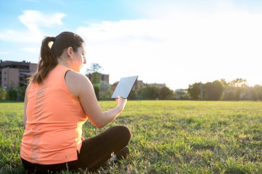 Güzel gökyüzü olan parkta tablet kullanan genç bir kadının arka plan görüntüsü